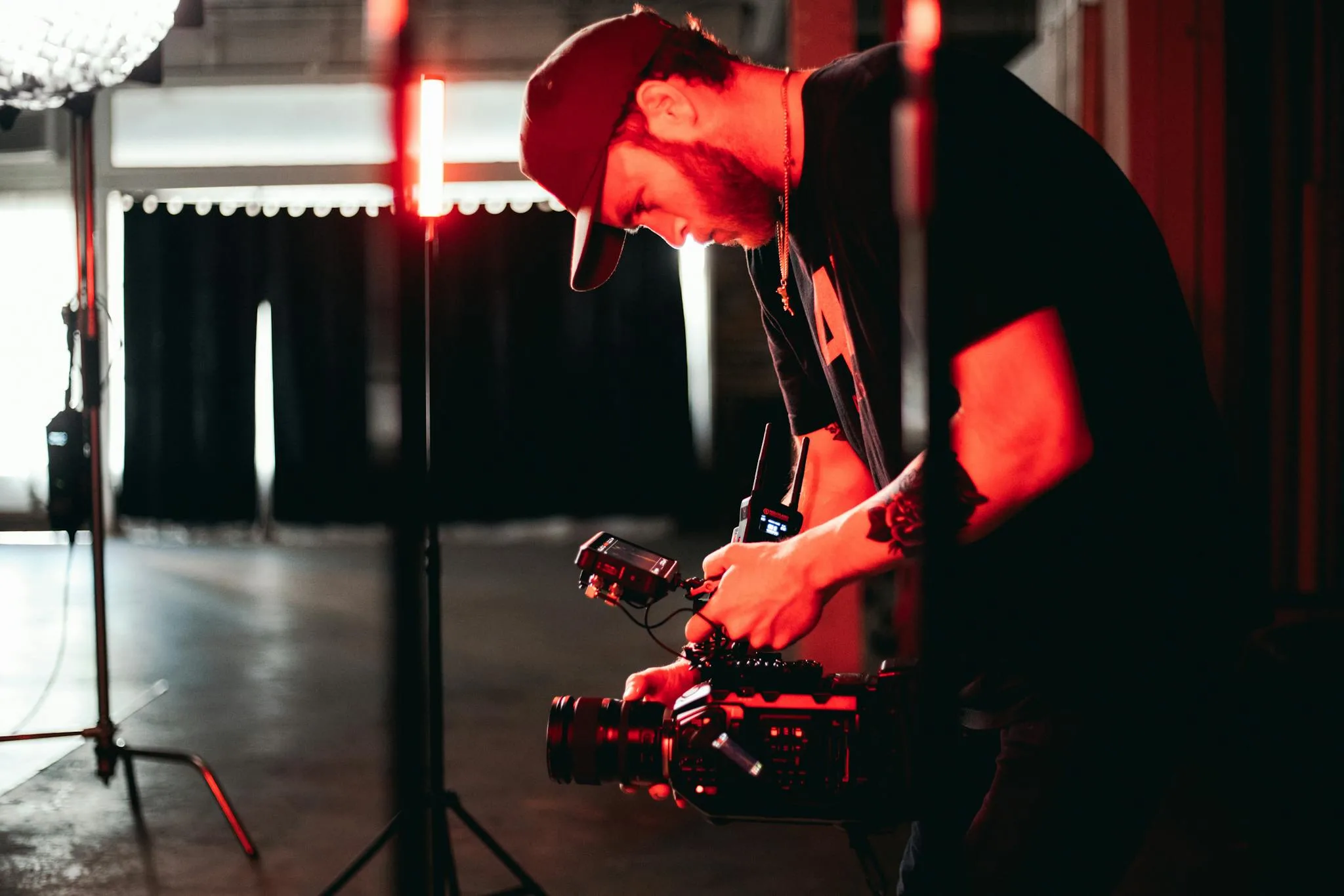 Male videographer adjusting camera equipment in an indoor studio setting with dim lighting.