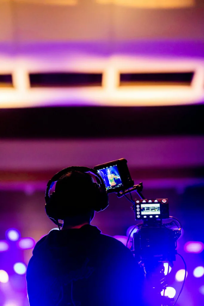 Silhouette of a videographer recording at a vibrant indoor concert event.